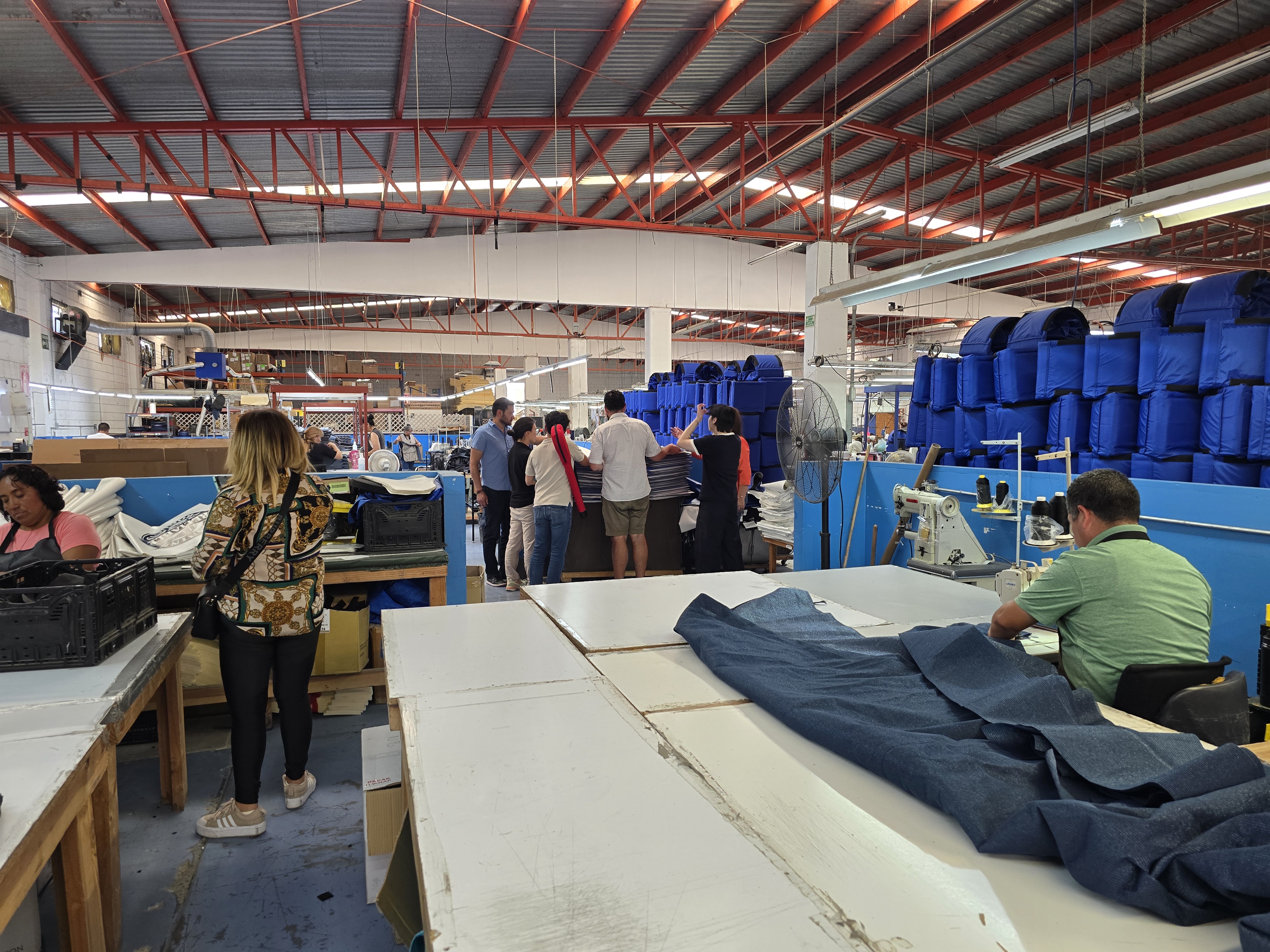 Factory floor with cutting tables, fabric, and finished product staging area in the Tijuana sewing facility